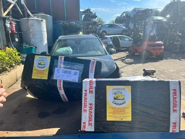 Auto parcheggiata nel vialetto accanto a grandi pacchi etichettati e avvolti in nastro adesivo grigio e rosa.
