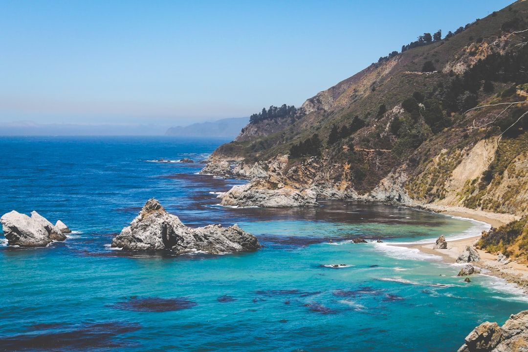 Rocky turquoise cove with sandy beach and steep coastal cliffs under a clear blue sky
