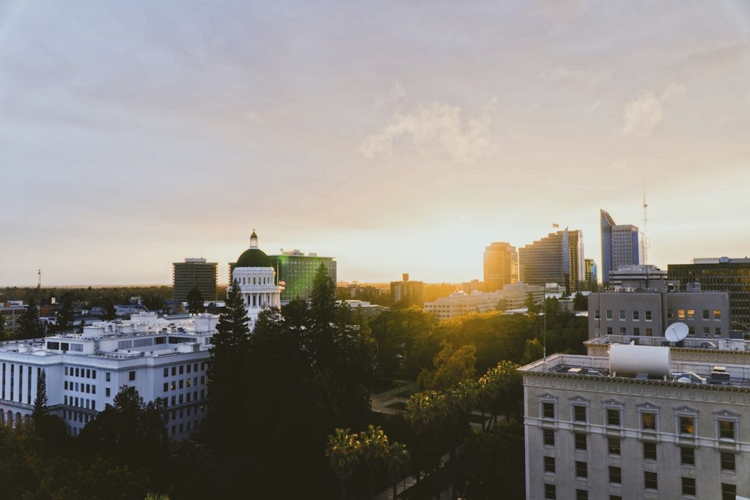 Sunset over a city skyline with trees and buildings silhouetted against a warm sky