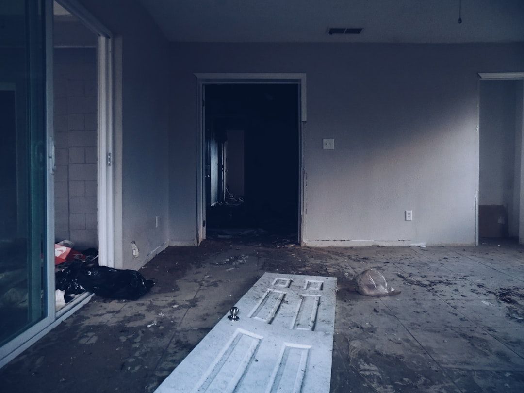 Empty, dimly lit room with bare walls, open doorways, and debris on the floor