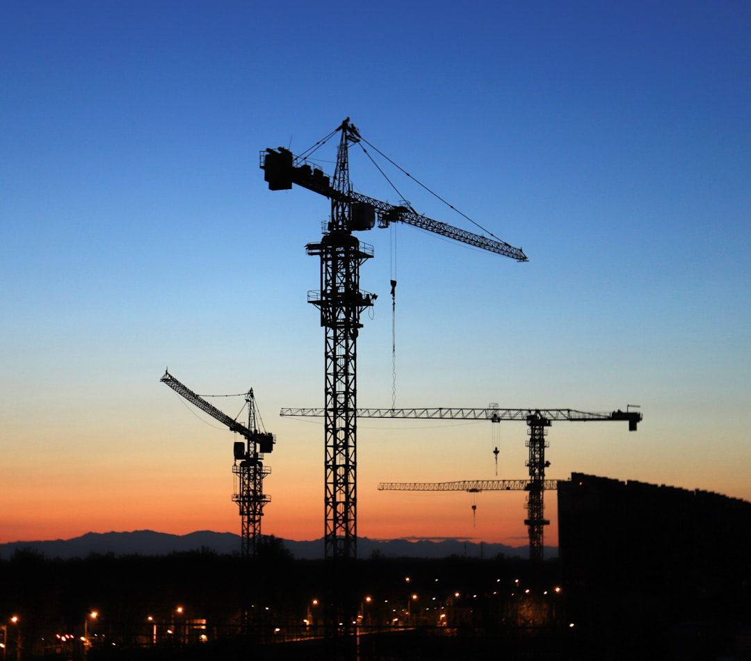 Silhouetted construction cranes against a sunset sky above city lights