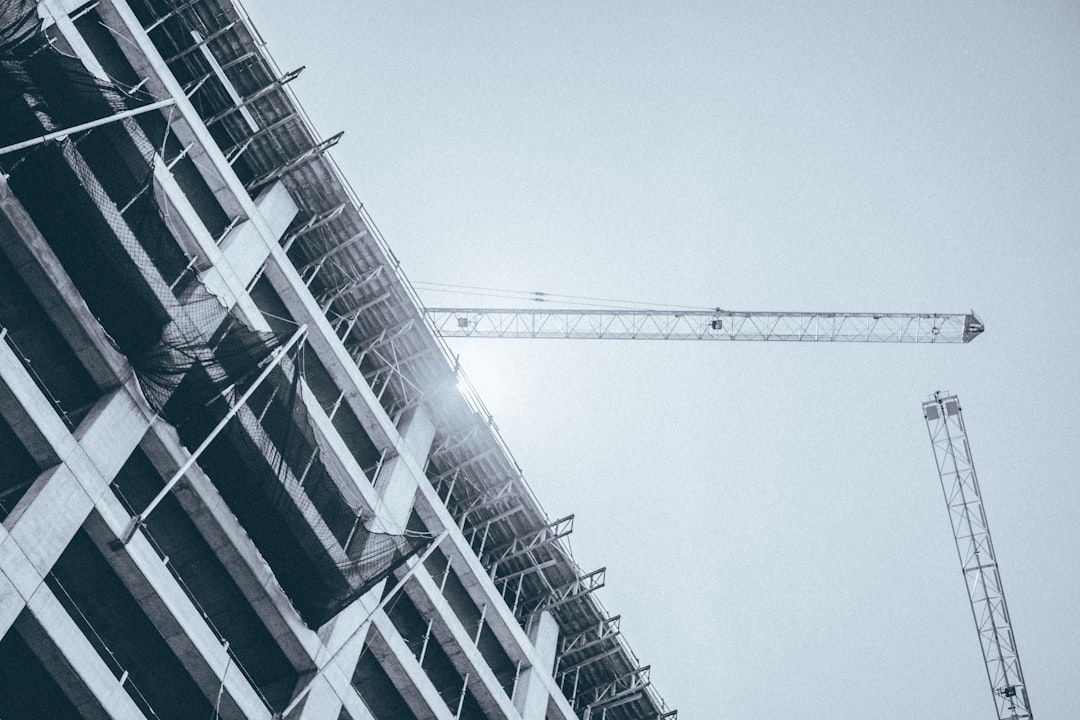 Upward view of a construction site with cranes and a partially built high-rise against a gray sky