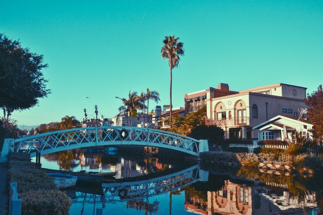 Canal with blue arched bridge, palm trees, and white buildings reflected in calm water at sunset