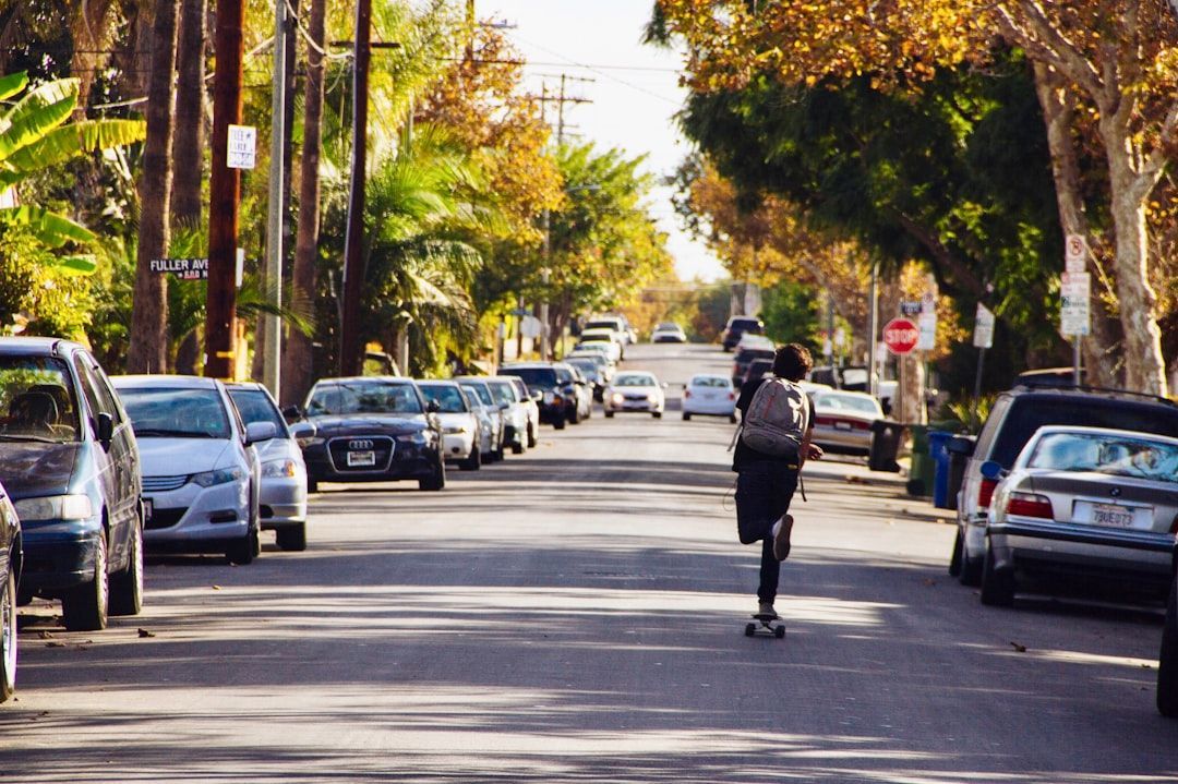 Person skateboarding down a tree-lined residential street with parked cars on both sides.