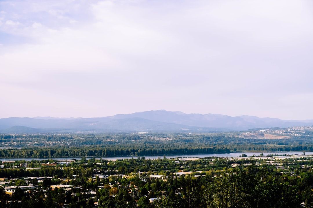 Wide landscape of a city and green fields beneath hazy mountains under a pale sky