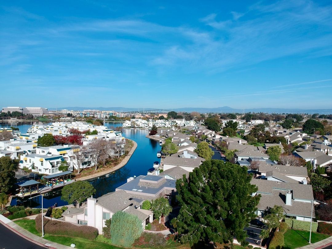Aerial view of a suburban neighborhood with a canal, rooftops, trees, and blue sky.