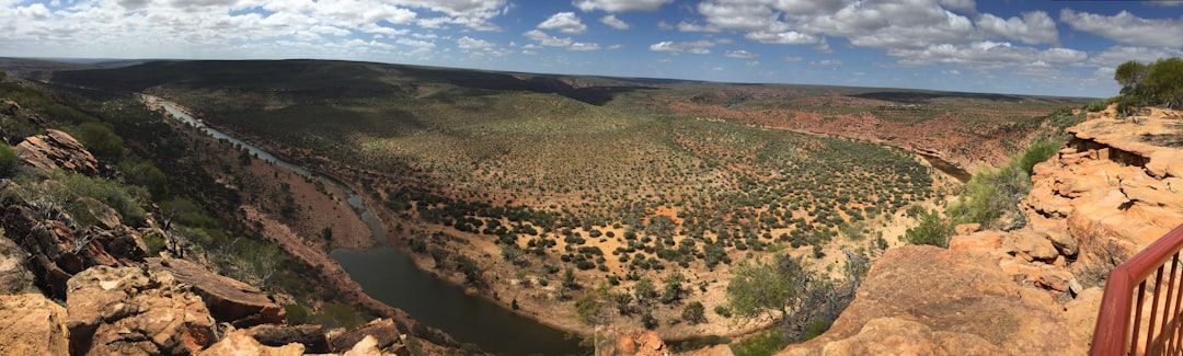 Panoramic view of a desert canyon with rocky cliffs, green valley floor, and cloudy blue sky