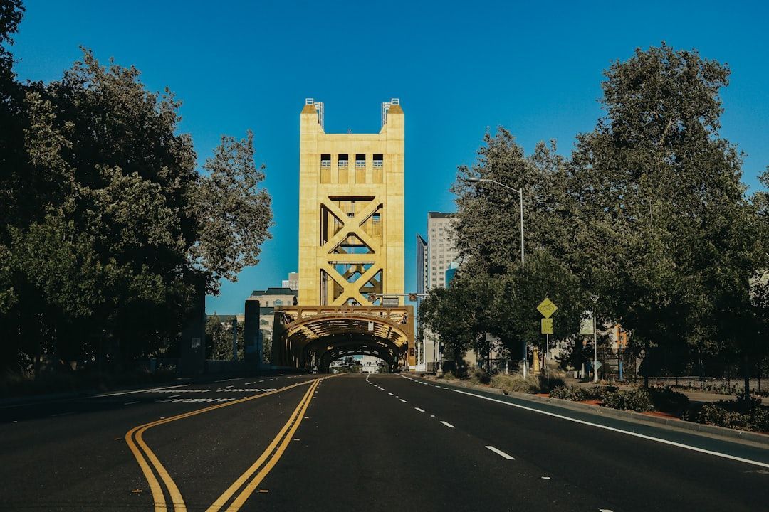 Yellow suspension bridge tower over a tree-lined road under a blue sky