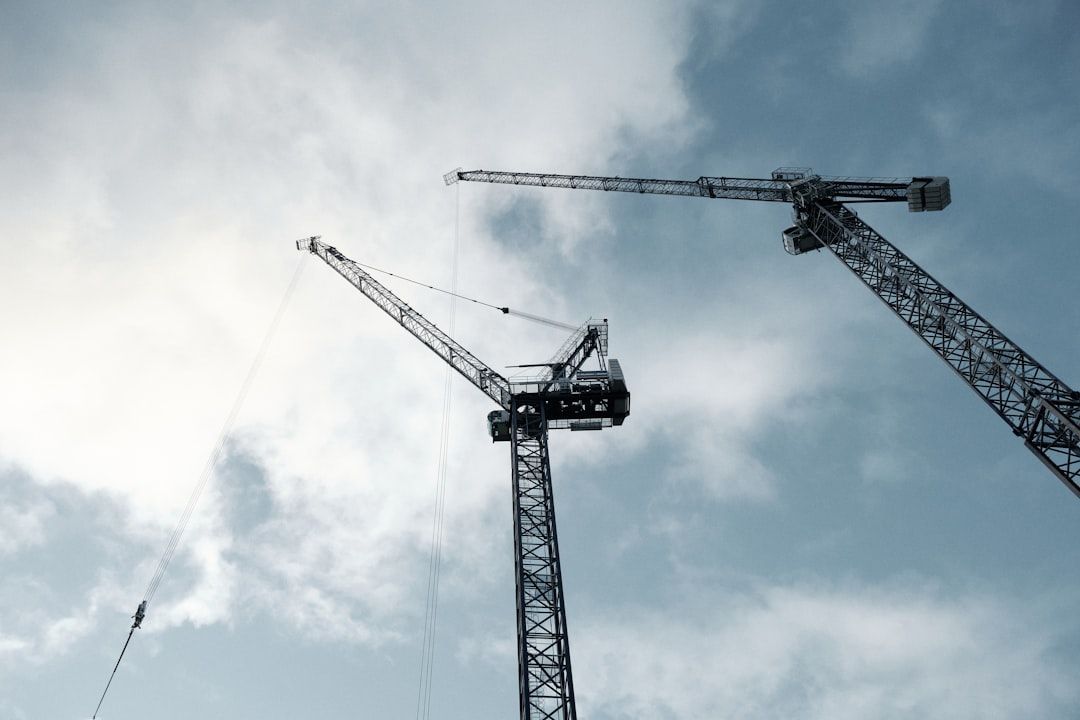 Two construction cranes against a cloudy blue sky