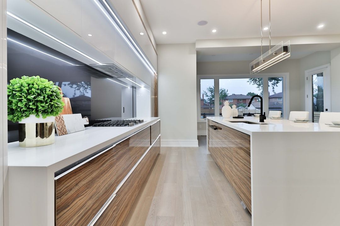 Modern white kitchen with wood accents, island counter, and large windows overlooking greenery