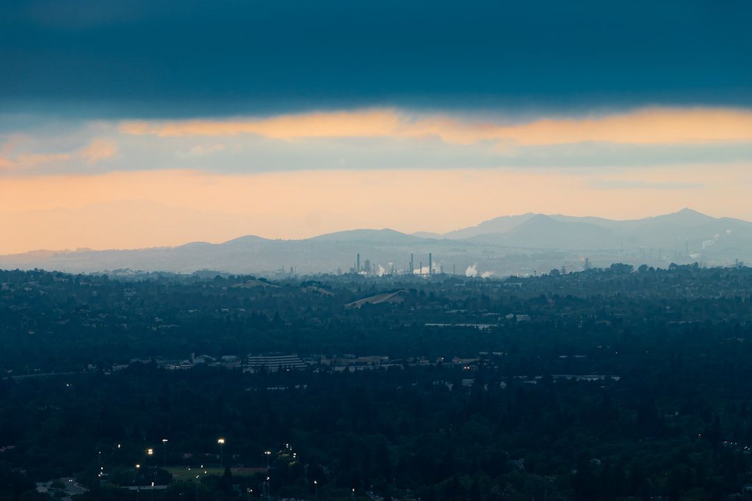 Hazy city skyline at dusk with mountains in the distance and a dramatic orange-blue sky