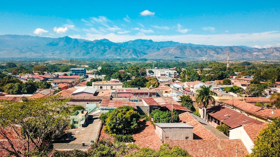 View over a town with red roofs and trees, backed by mountains under a clear blue sky