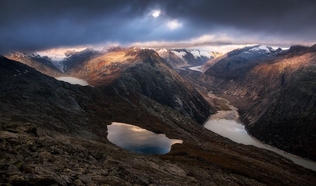 Snowy mountain valley with a winding river, two lakes, and dramatic clouds at sunrise