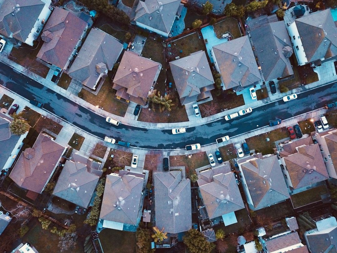 Aerial view of suburban rooftops along a curved residential street with parked cars and trees.