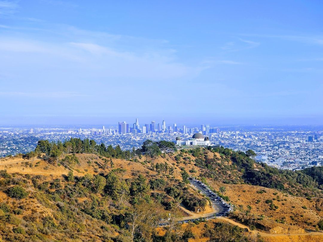Dry hillside with a winding path overlooking a distant city skyline under a clear blue sky