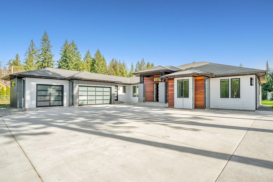 Modern single-story house with a two-car garage, white siding, and a concrete driveway under a clear blue sky