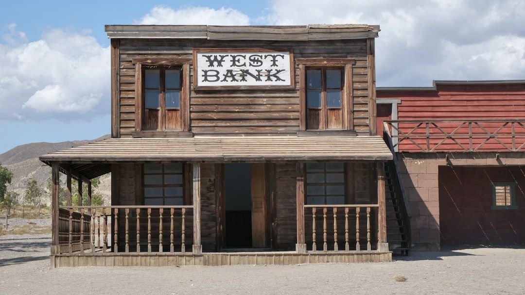 Old west bank building with wooden porch and a “WEST BANK” sign under a blue sky.