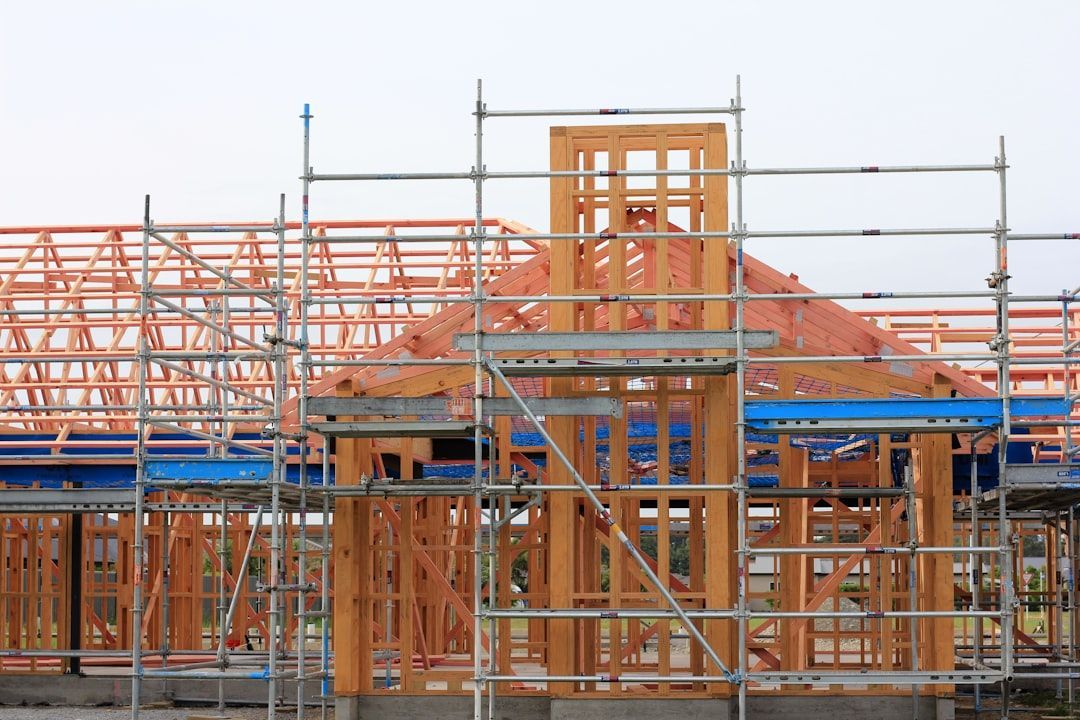 Scaffolding around a partially built house with orange framing and blue roofing under construction