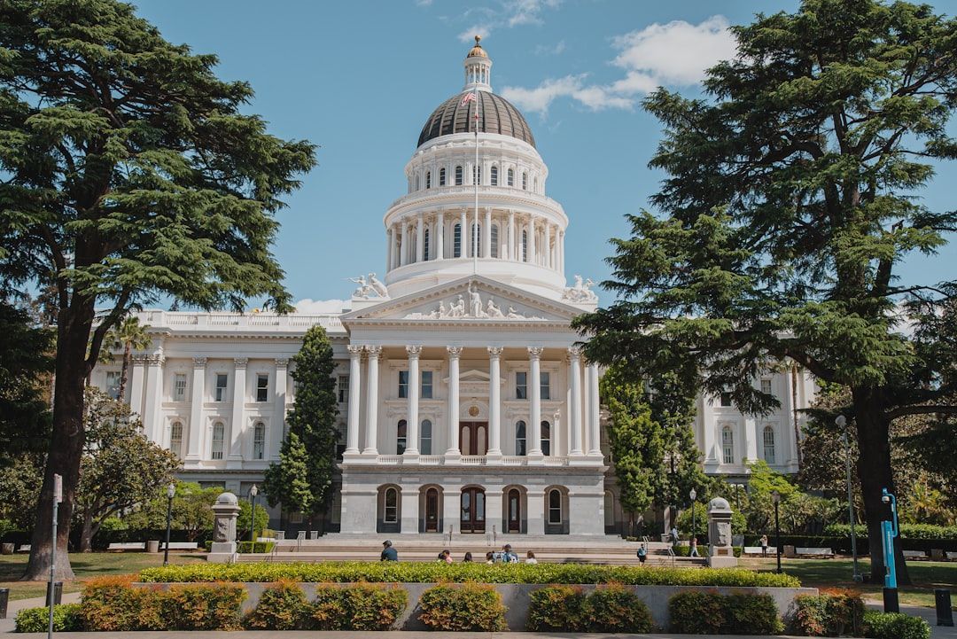 Historic white capitol building with a central dome, framed by trees and gardens under a blue sky