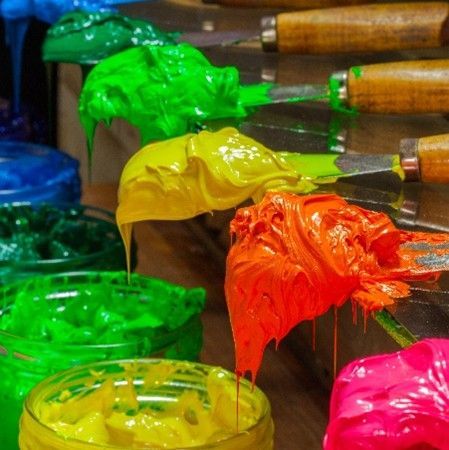 Paintbrushes loaded with bright green, yellow, orange, and pink paint in a studio setting