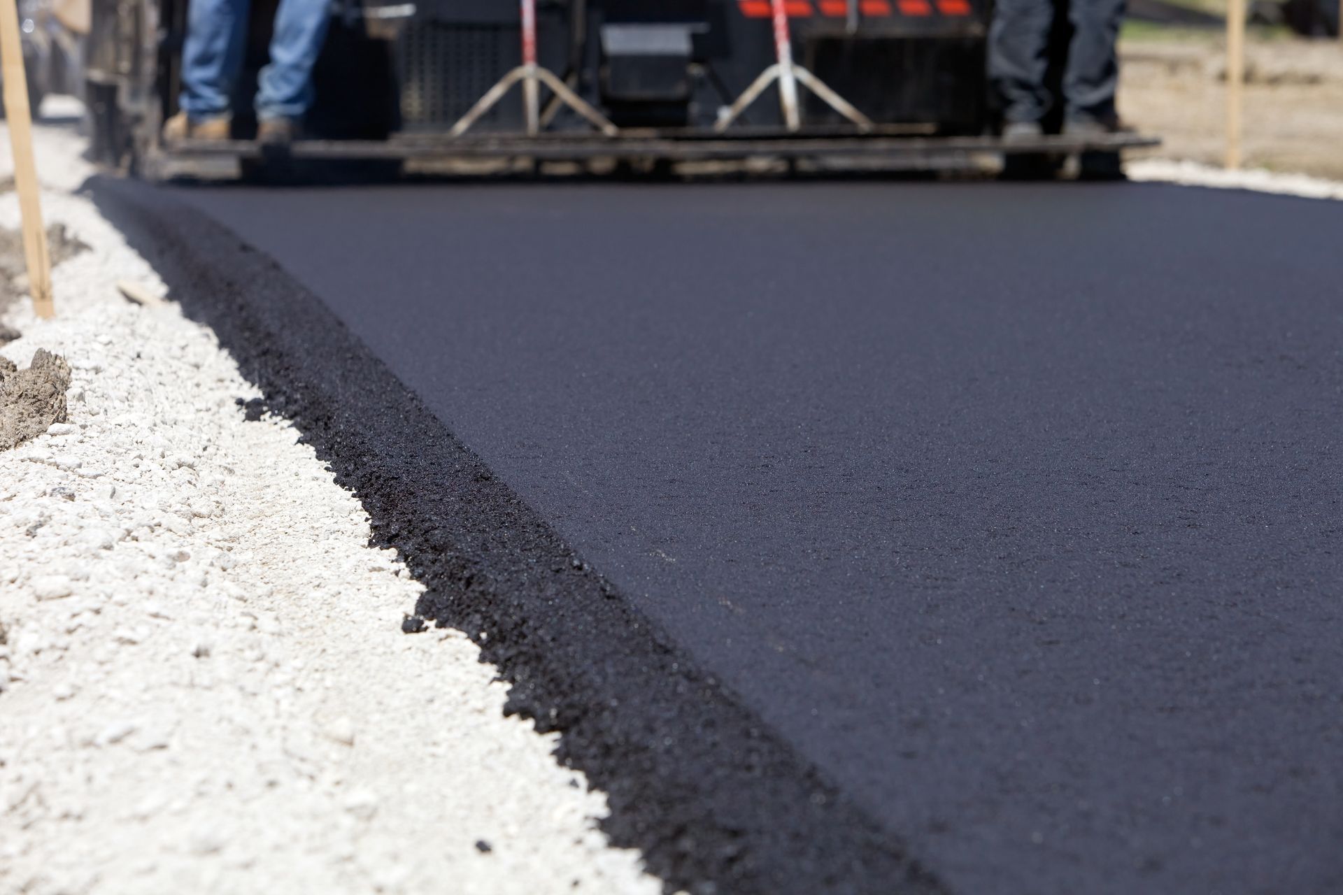 Road paving in progress; asphalt being laid by a machine, with workers standing near it.