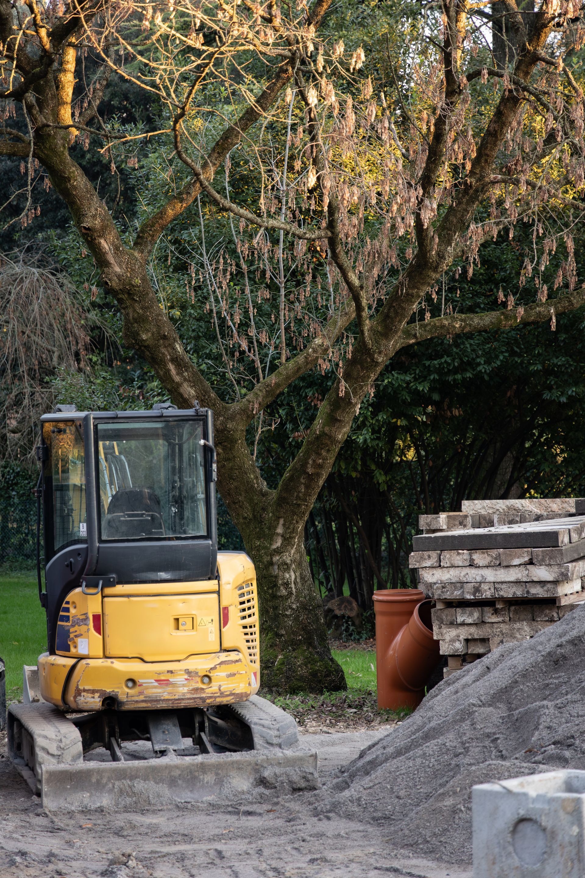 Commercial paving contractor operating excavator near gravel and stacked materials on site.