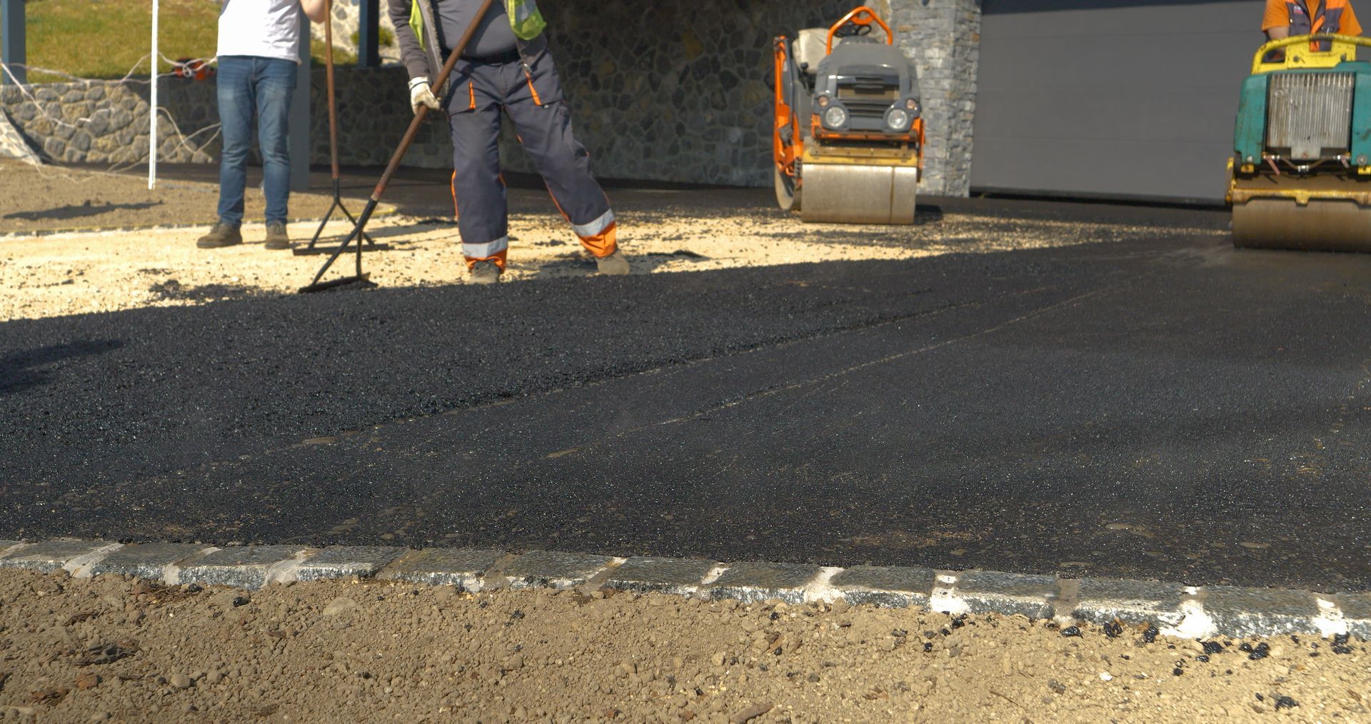 Paving crew spreading fresh asphalt as a roller compacts a new driveway.