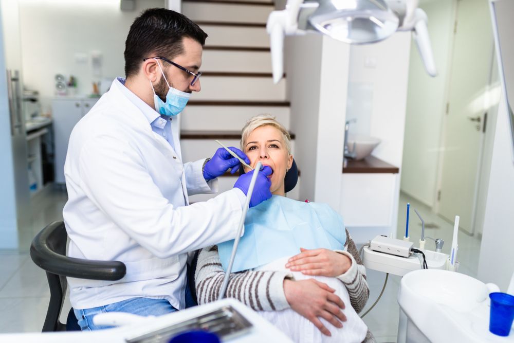 A dentist is examining a woman 's teeth in a dental office.