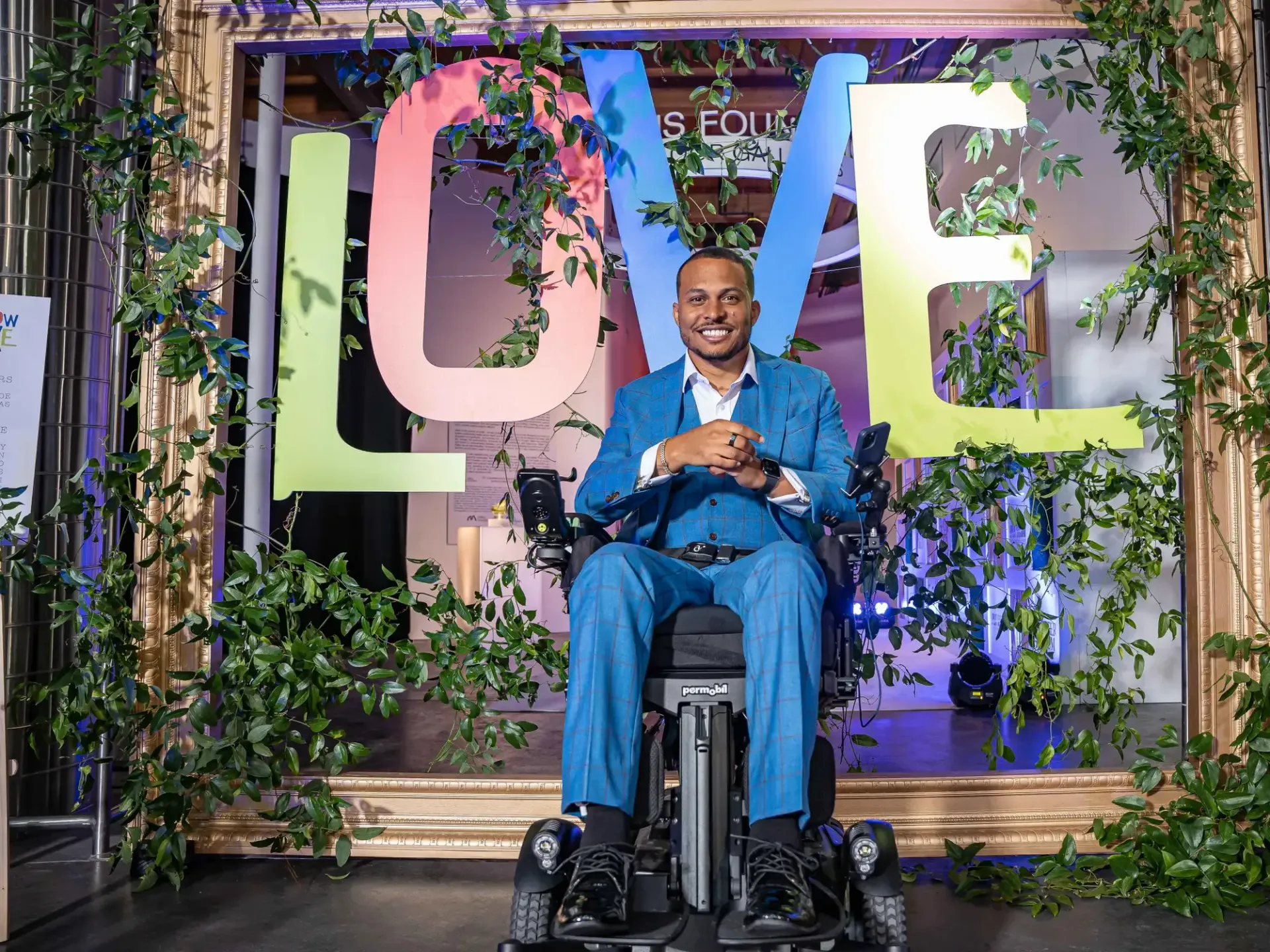A man in a suit is sitting in a wheelchair in front of a sign that says love.