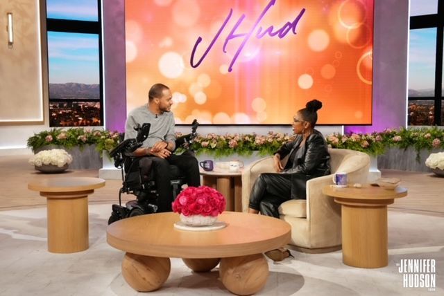 A man in a wheelchair is talking to a woman on a television show