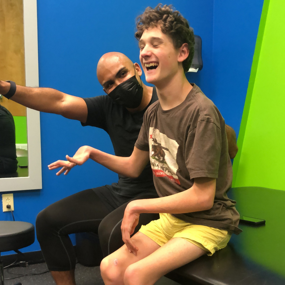 A man wearing a mask is sitting next to a boy sitting on a bench