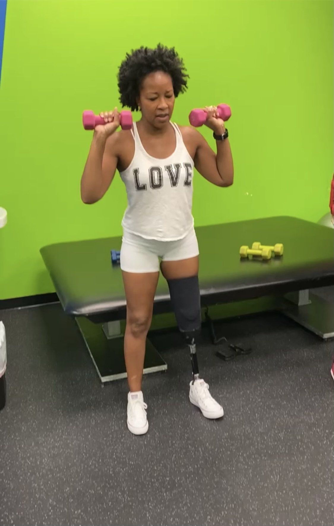 A woman with a prosthetic leg is lifting dumbbells in a gym.