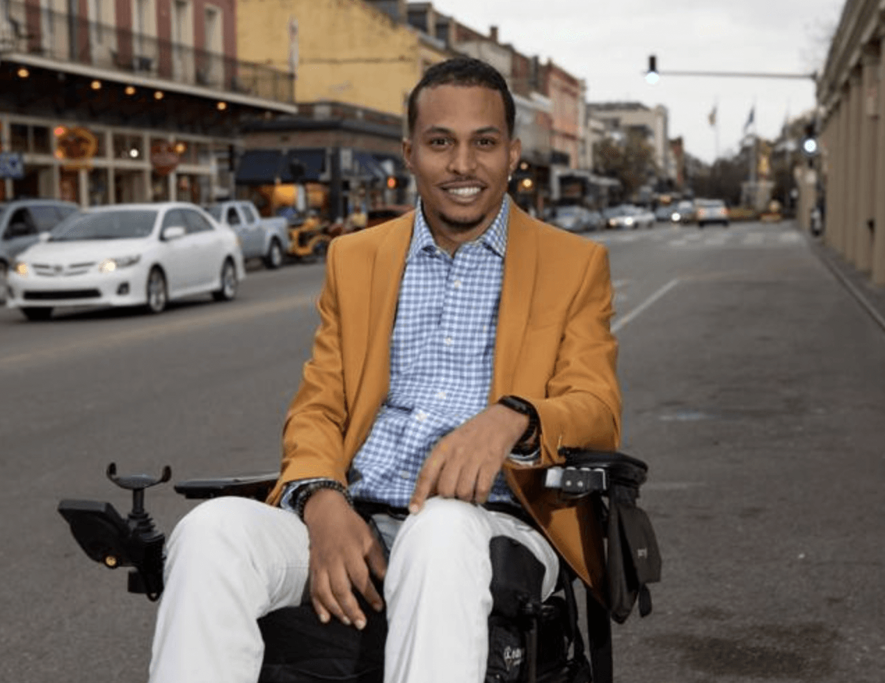 A man in a yellow jacket is sitting in a wheelchair on a city street.