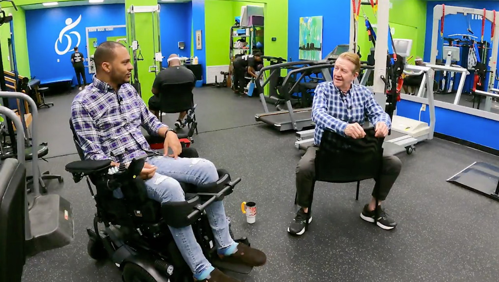 A man in a wheelchair is sitting next to another man in a chair in a gym.