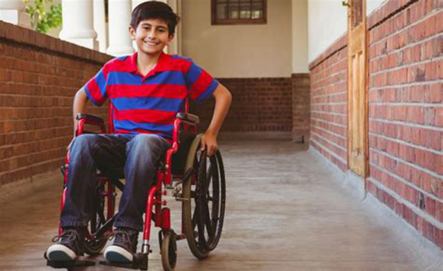 A young boy is sitting in a wheelchair in a hallway.