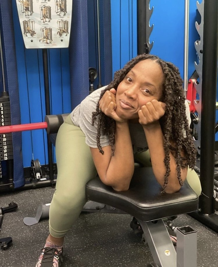 A woman is sitting on a bench in a gym with her hands on her face.