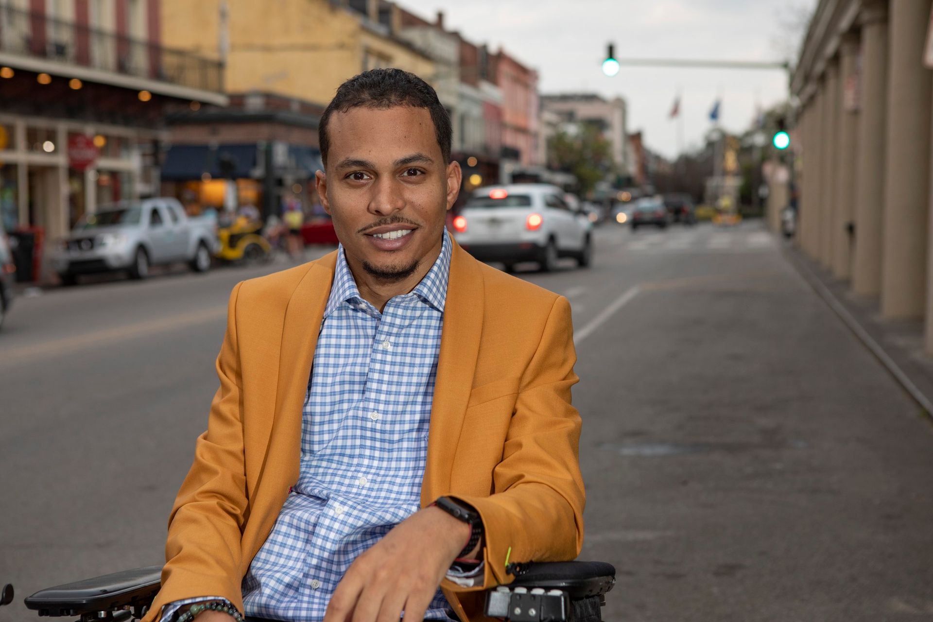 A man in a yellow jacket is sitting in a wheelchair on a city street.