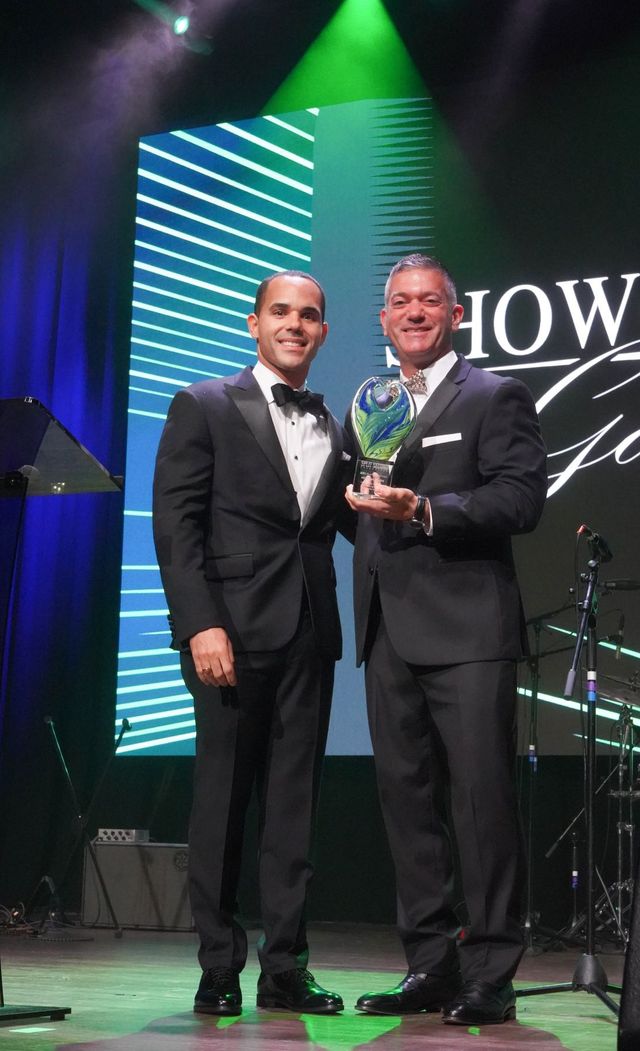 Two guests in tuxedos on stage, one holding a glass Show of Love award.