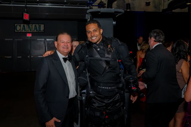 Mark Raymond Jr., in an exoskeleton, smiles with a guest during the gala.