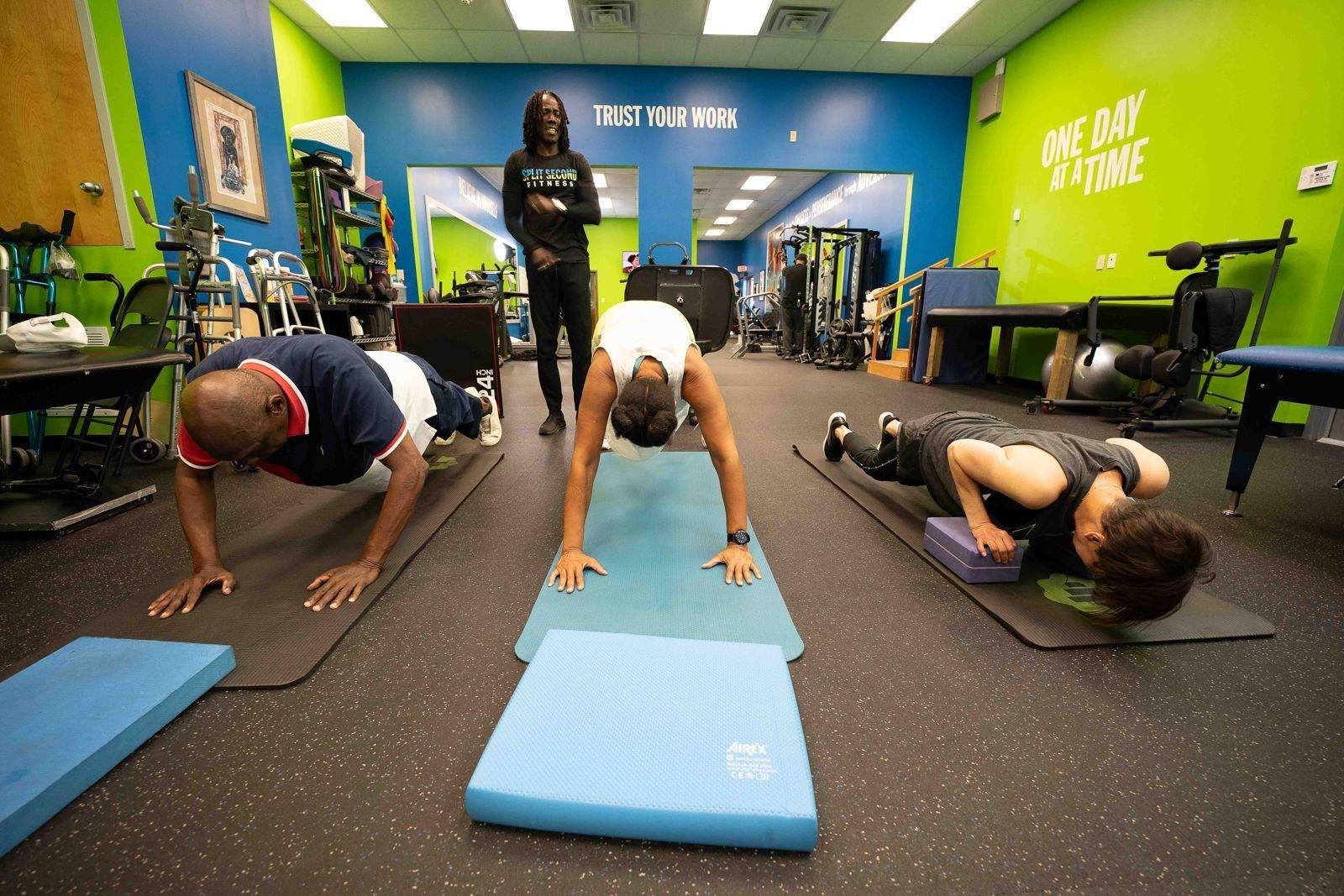 Three members hold plank and push-up positions on mats during a group class led by a coach