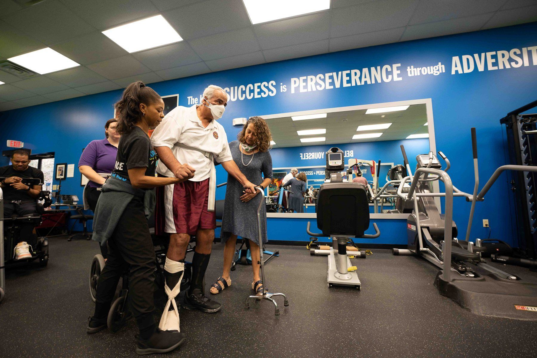A specialist and a family member support a member as he walks with a cane on the training floor.