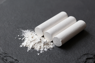 Tres tizas blancas con polvo de tiza sobre una superficie de pizarra oscura