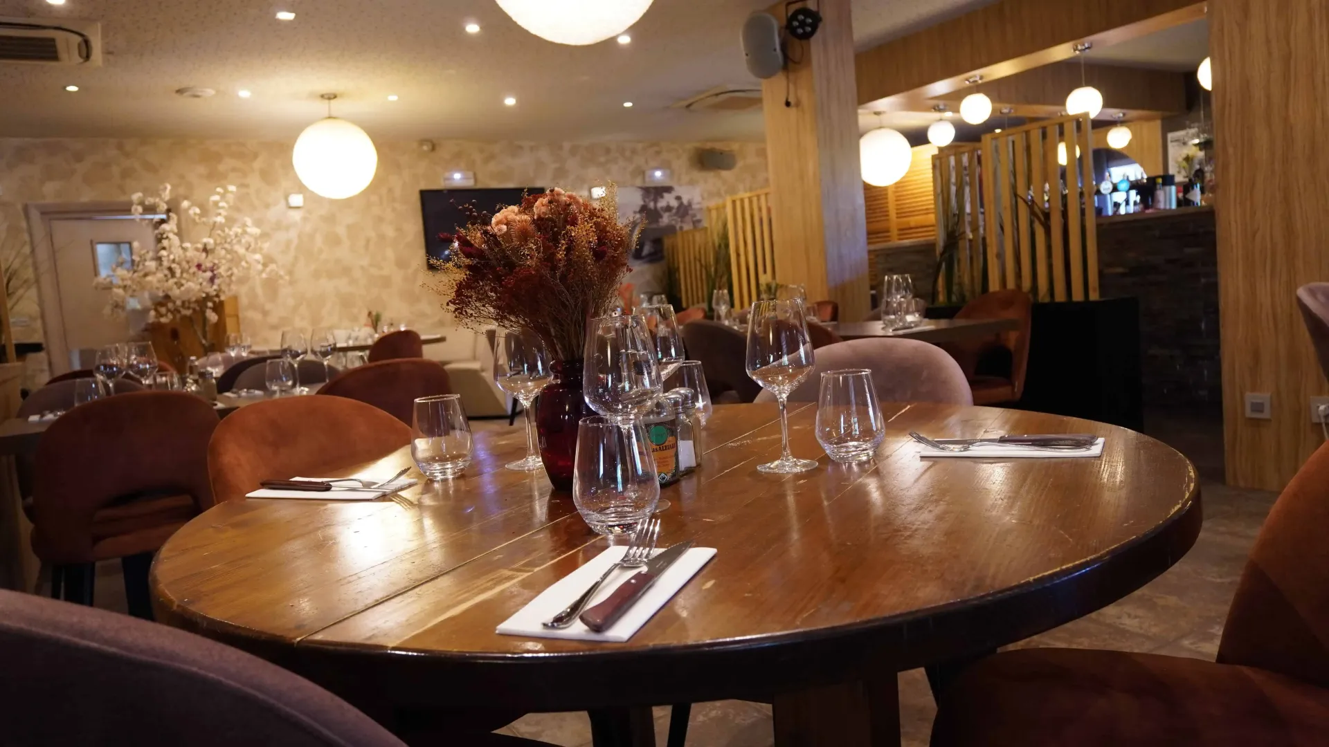 Une table ronde en bois dressée pour les convives dans un restaurant chaleureux à l'éclairage tamisé, avec des chaises et un décor en velours moelleux.