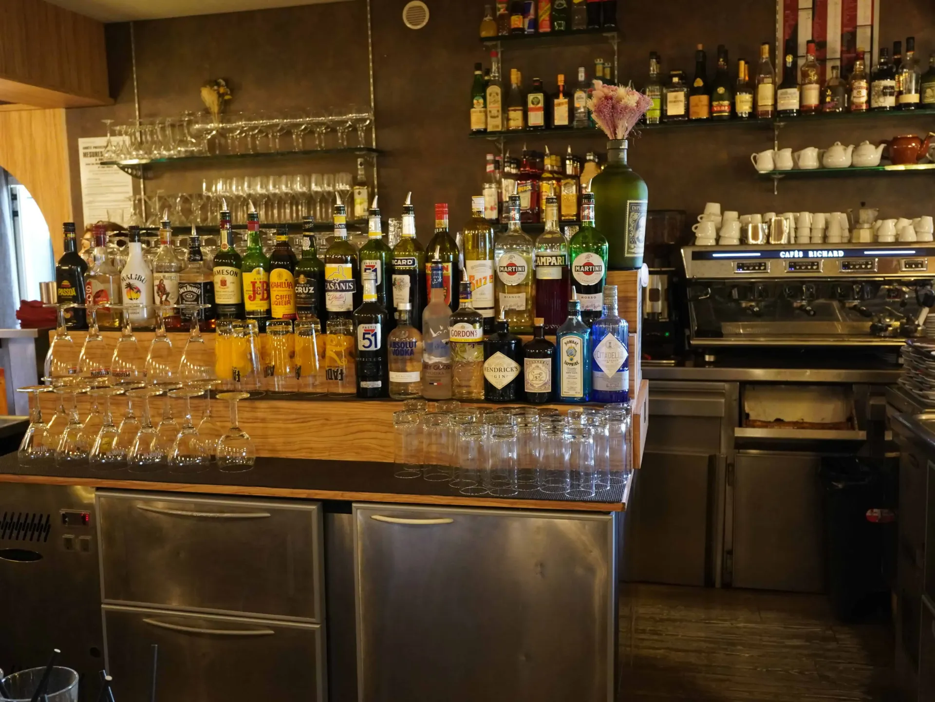 Un comptoir de bar commercial avec des étagères garnies de diverses bouteilles d'alcool, de verres et d'une machine à expresso.