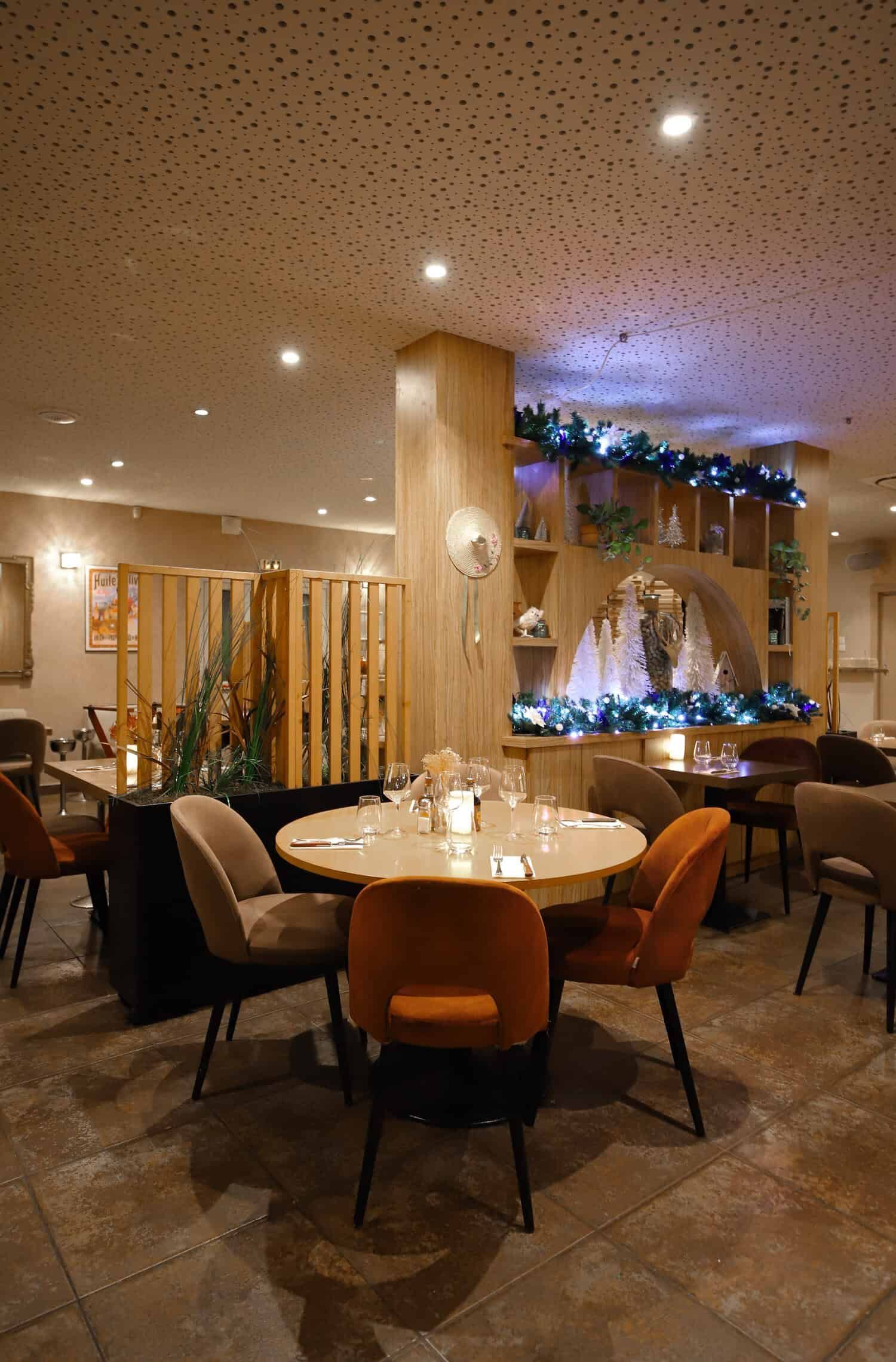 L'intérieur d'un restaurant à l'éclairage chaleureux présente une table ronde entourée de chaises beiges et orange sur un sol carrelé.