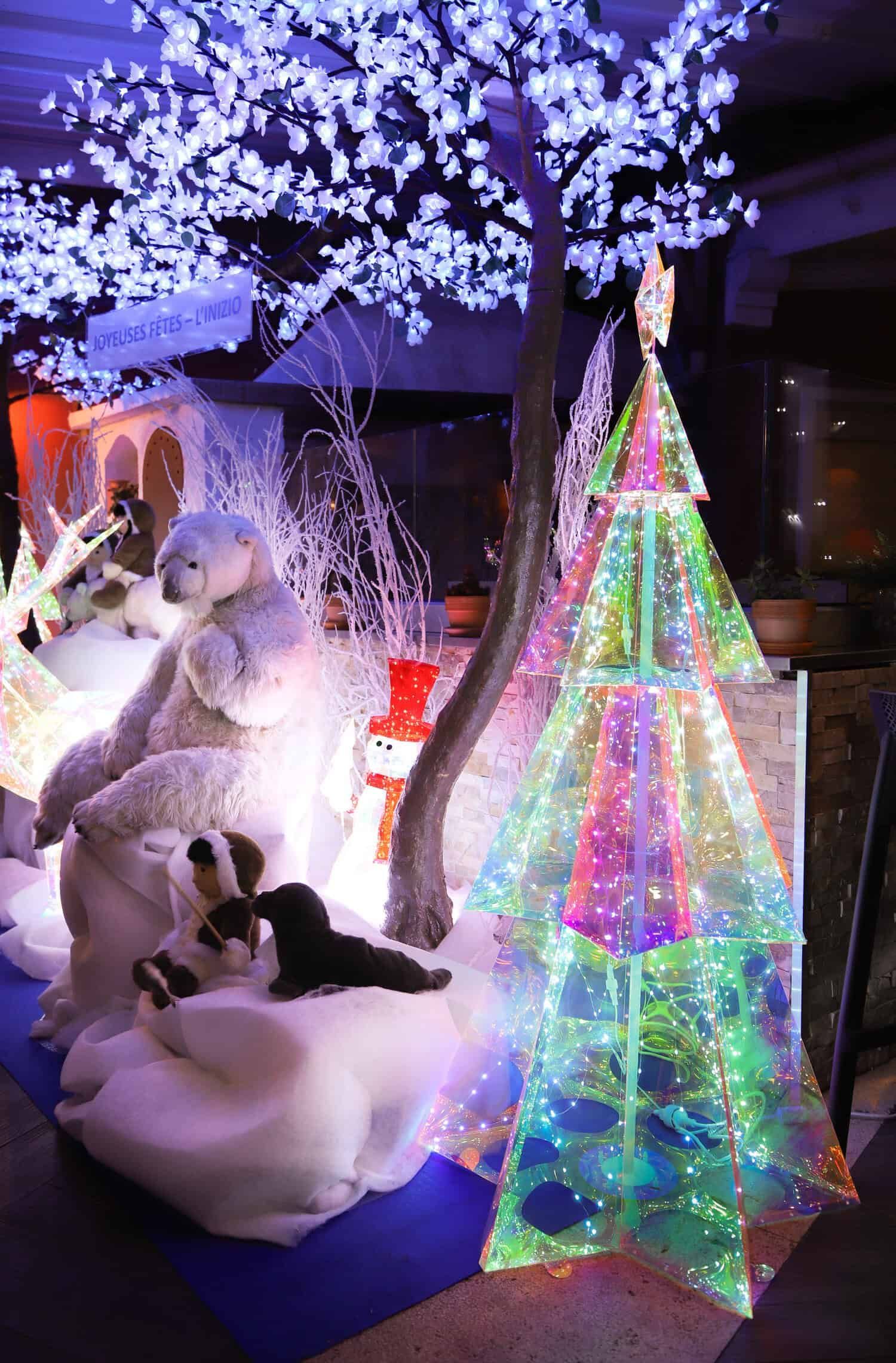 Une décoration festive avec un ours polaire blanc, un petit animal sombre et un sapin de Noël triangulaire multicolore illuminé.