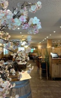 Un cerisier en fleurs décoratif au premier plan d'un intérieur de restaurant chaleureux et tamisé, avec des tables en bois.