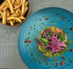Une assiette bleue contenant une salade gourmande garnie d'oignons rouges marinés et de graines de grenade, servie avec des frites.