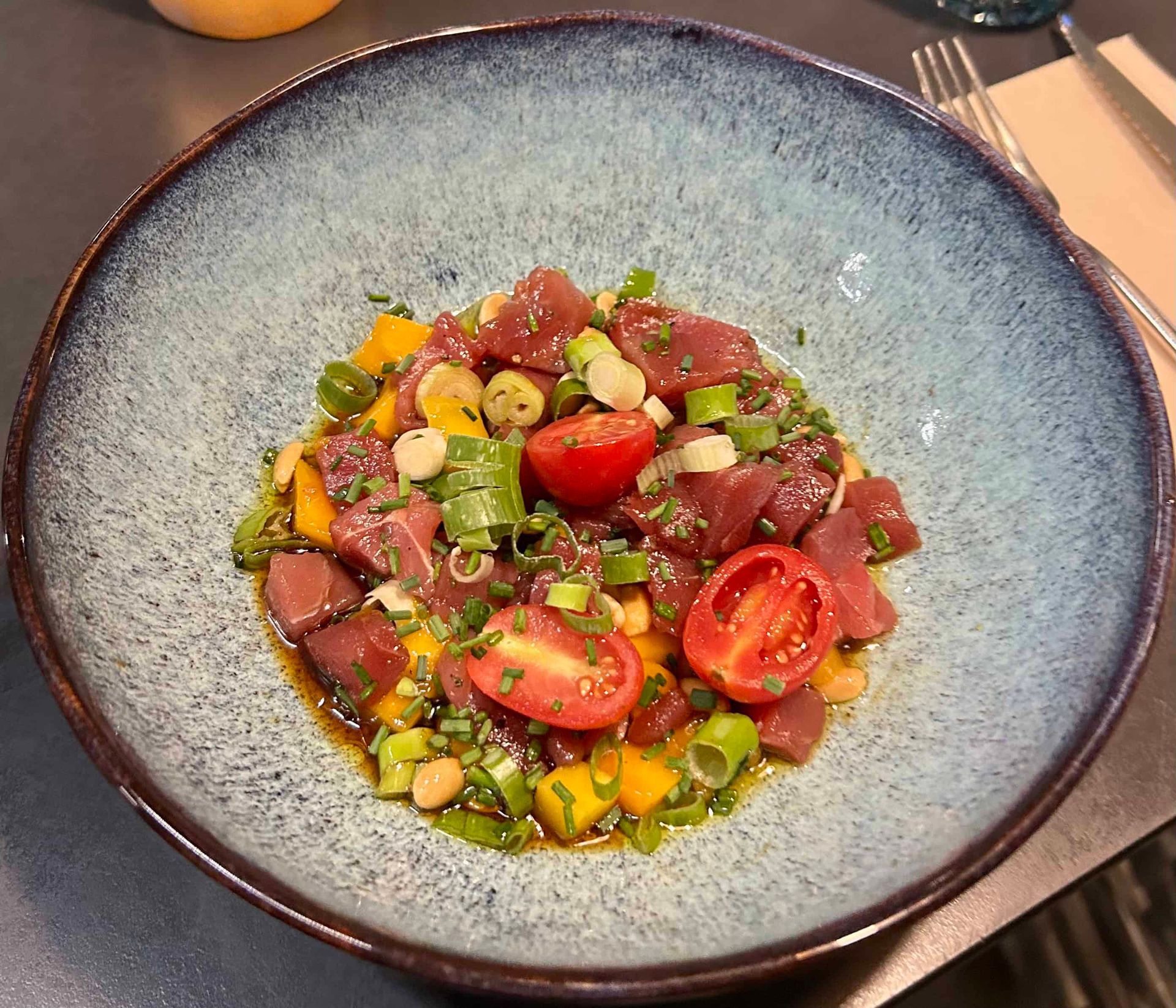 Un bol de poke au thon ahi composé de cubes de thon cru, de mangue jaune coupée en dés, de tomates cerises et d'oignons verts émincés.