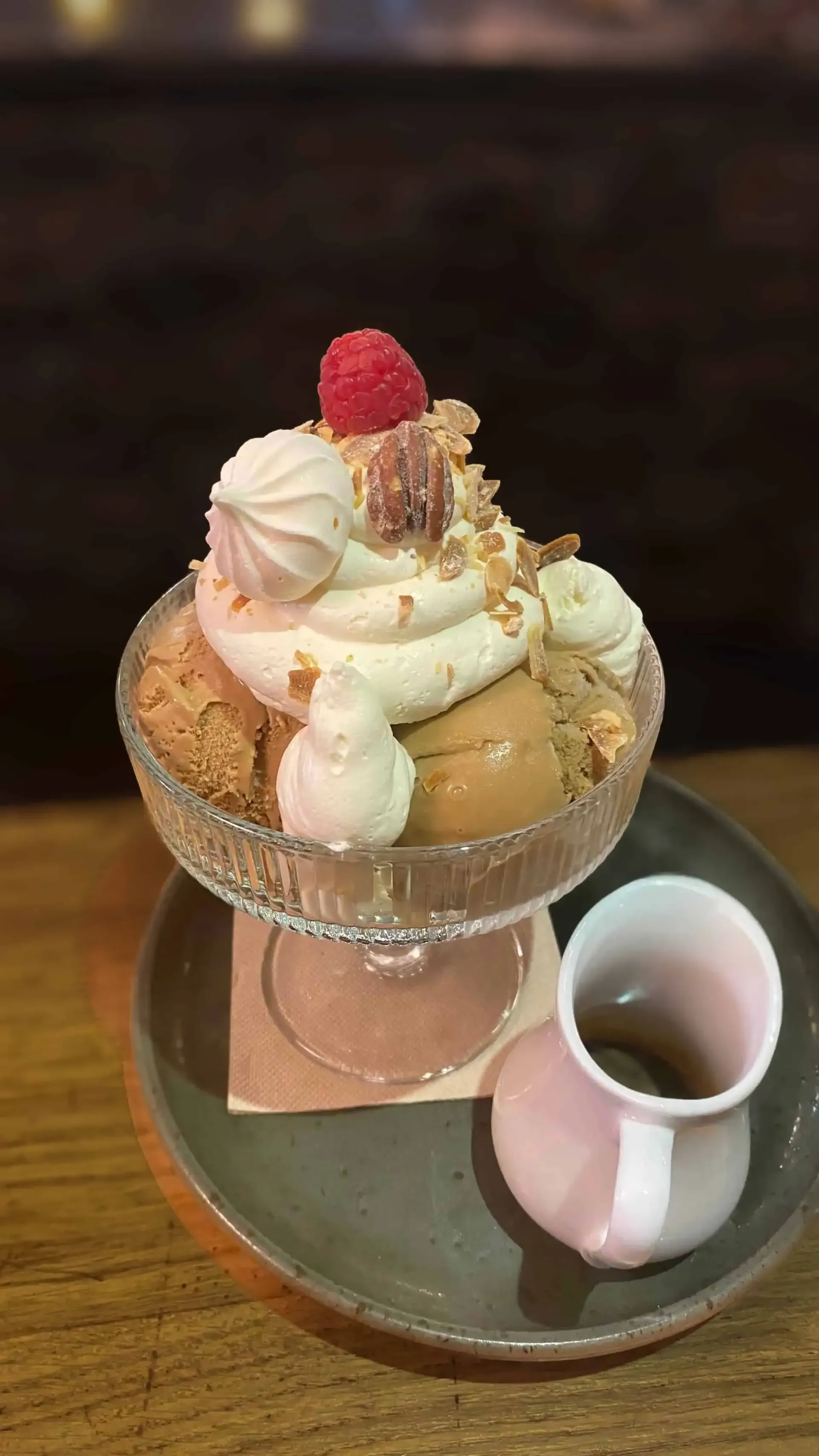Une coupe à dessert en verre garnie de crème fouettée, d'une framboise et de meringue, servie avec un petit pichet d'accompagnement sur un plateau.